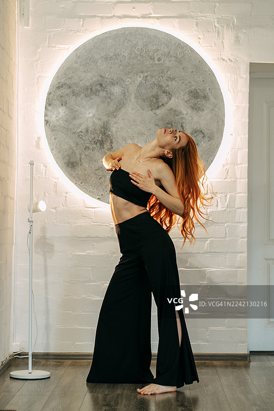 红发女子高举双臂，在月亮艺术装置前跳舞图片素材