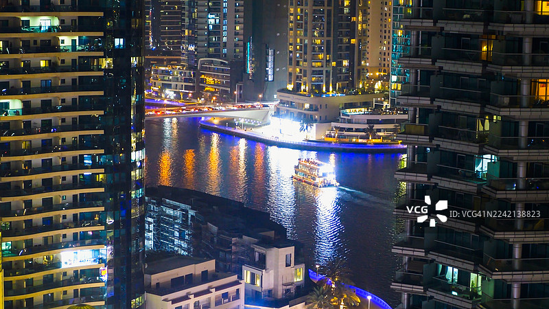 迪拜码头 - 灯火辉煌的船只在摩天大楼间穿梭，倒映在城市夜光下的运河水面上。图片素材