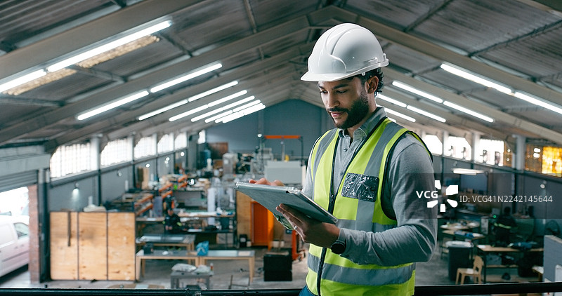 工程师，在线操作，男子手持平板电脑，在仓库进行网站上的绩效审查和生产。头戴安全帽，通过科技进行阅读、研究，以实现质量控制、生产和安全。图片素材