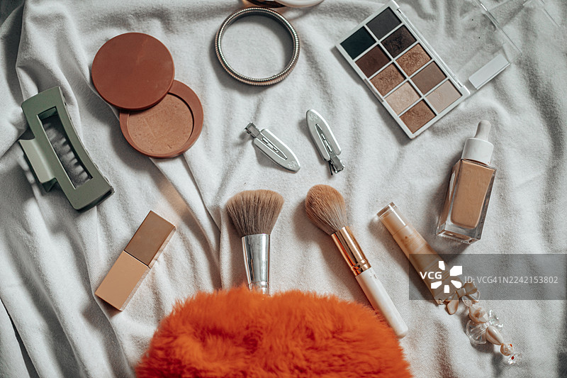 化妆包的平面图，里面装满了刷子、腮红、润唇膏、面霜和粉底等美容必需品。有条理的构图和柔和的光线突出了现代化妆品的质地和色彩，营造出时尚而女性化的外观。完美图片素材