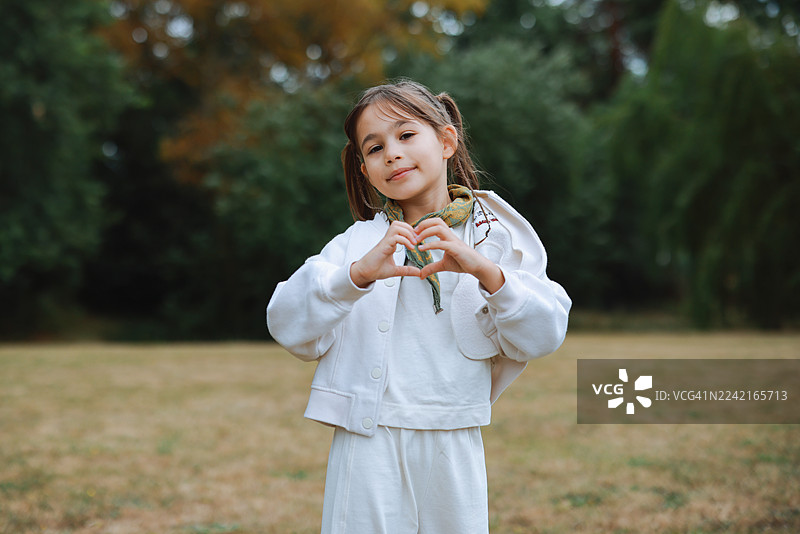 可爱的小女孩在阳光下的田野里用双手比心图片素材