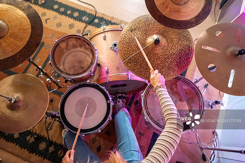 从上方俯视，一名年轻女子在紫色灯光下的音乐工作室里打鼓的手图片素材