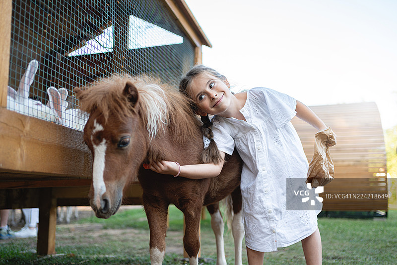 小女孩穿着白裙子在草地上拥抱小马图片素材