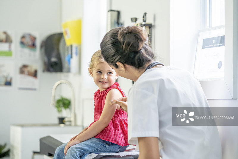 温柔的儿科检查时刻，一位充满关怀的医生正在为一位微笑的小女孩在明亮的诊所里进行检查图片素材