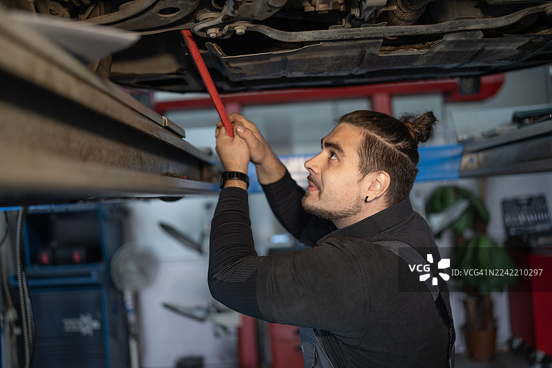 专业技师在汽车修理厂用红色工具在升降机下检查汽车图片素材