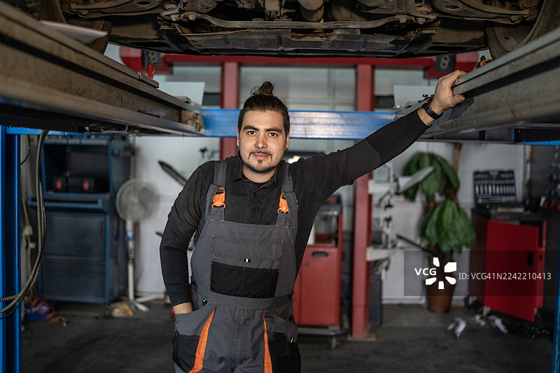 穿着工作服的机械师在汽车修理厂的汽车升降机下摆出姿势图片素材