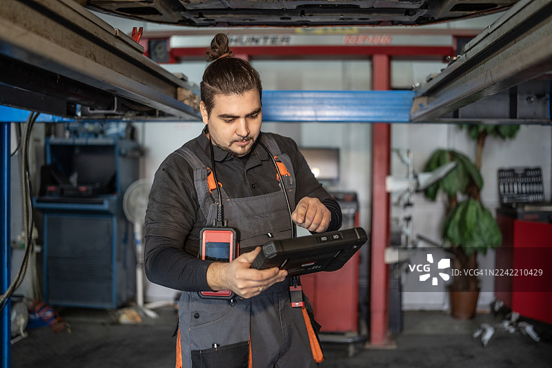 汽车修理厂里，机械师在汽车举升机下方使用诊断平板电脑图片素材