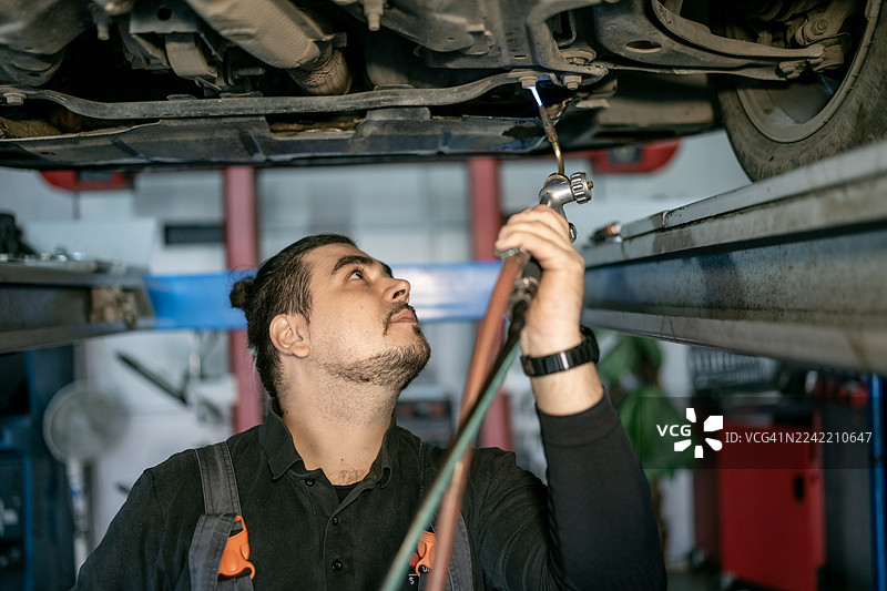 汽车修理工在汽车修理店的升降机下使用工具进行维护和修理工作图片素材