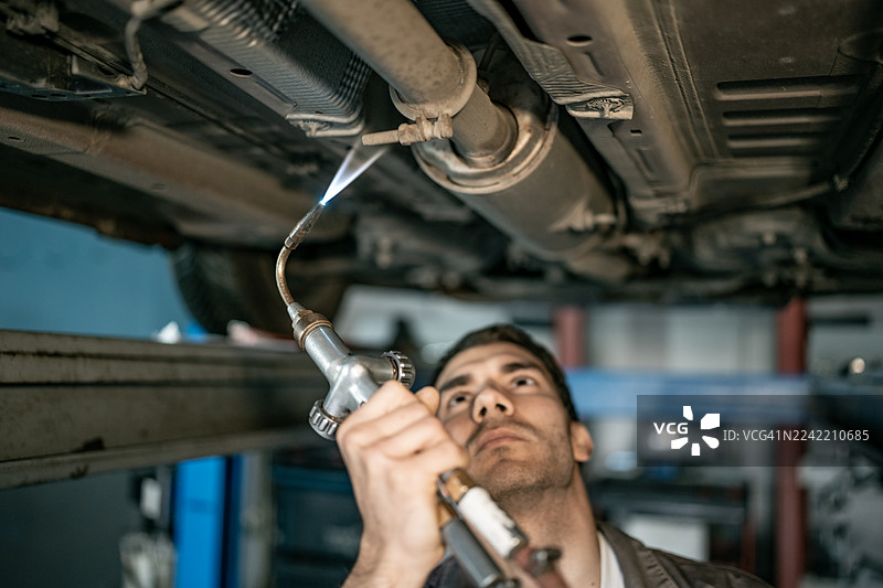 修理工在车间对着汽车底部使用焊枪进行汽车维修图片素材
