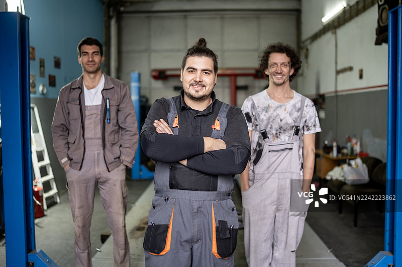 自信的汽车修理团队在车间合影，提供保养和维修服务，专业的车库肖像图片素材