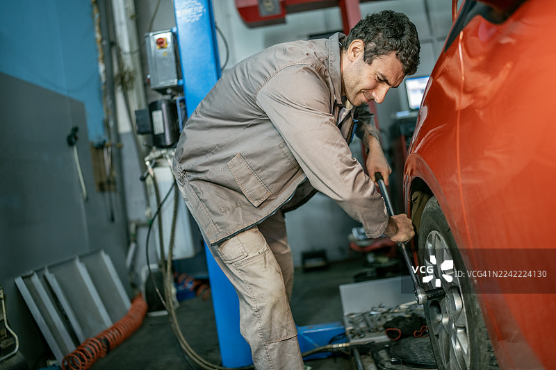 汽车修理店里正在更换汽车轮胎的机械师，专注的汽车维修场景图片素材