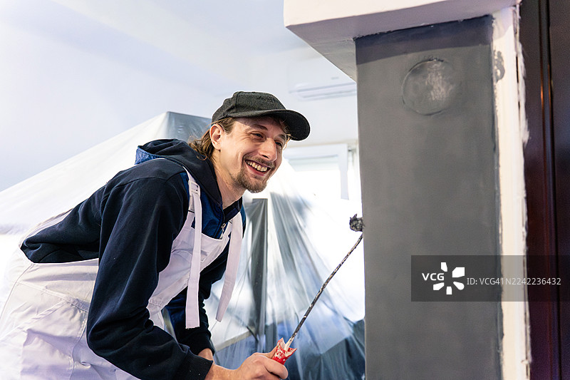 穿着白色围裙的快乐油漆工正在明亮现代的空间里进行室内翻新图片素材