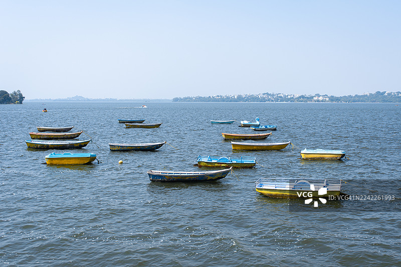 平静湖面上色彩鲜艳的船只，天空晴朗，远方是城市天际线的高角度视图图片素材
