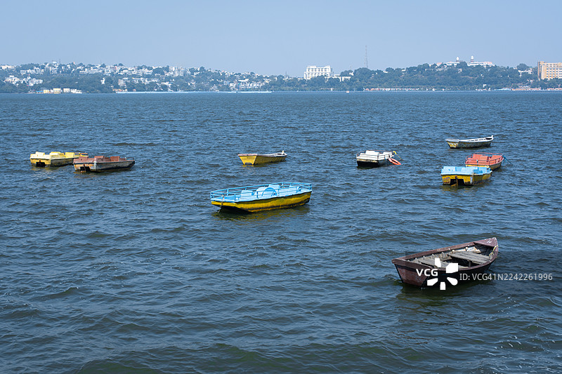 晴朗的一天，城市天际线在背景中，从高处俯瞰，可以看到广阔的蓝色湖面上漂浮着许多色彩缤纷的小船。图片素材