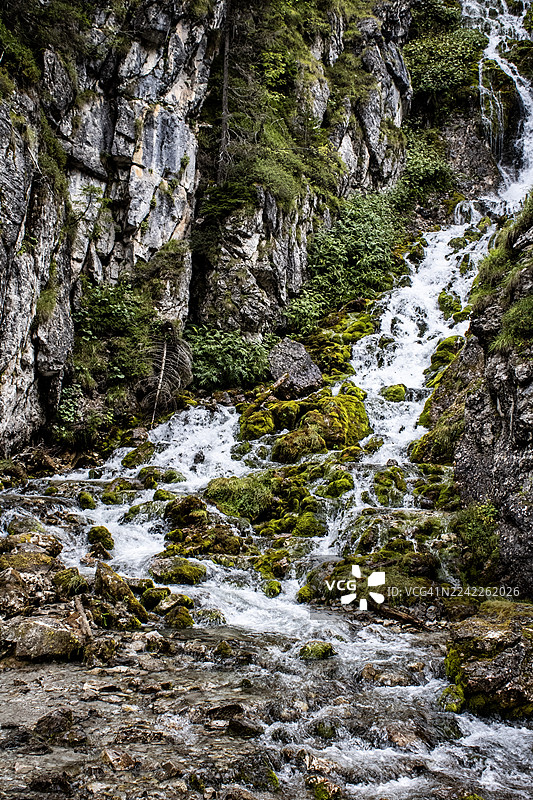 充满活力的溪流从崎岖的山坡上流淌而下，越过长满苔藓的岩石，展现了自然的伟力图片素材