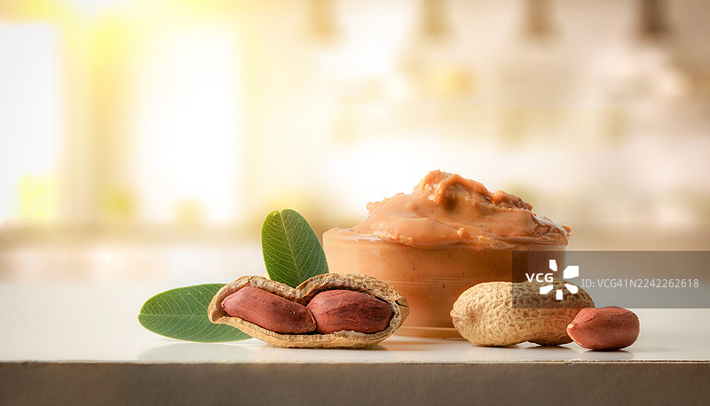 白色背景上，碗中盛有新鲜的花生酱，旁边散落着带壳和去壳的花生以及绿叶，特写镜头。图片素材
