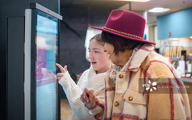 宾夕法尼亚州波科诺地区一家快餐店里，一位74岁的老妇人和一位11岁的女孩正在使用自助点餐机。图片素材