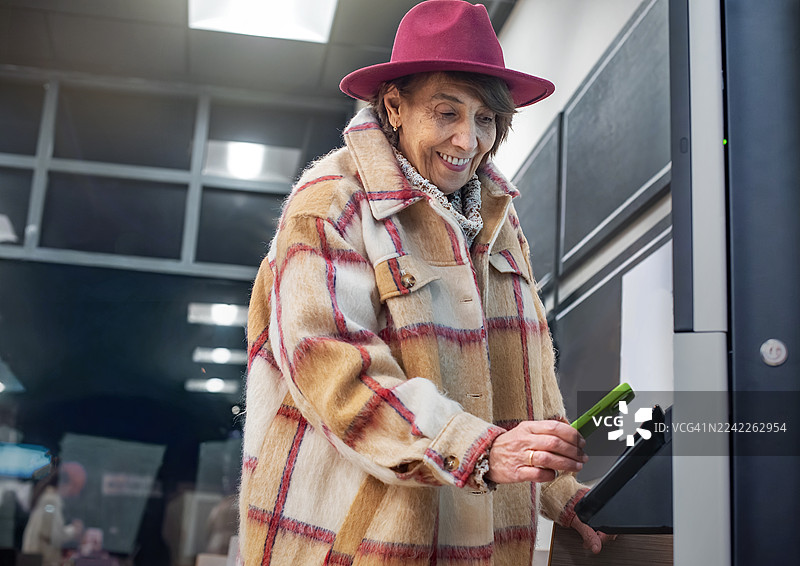 一位时髦的老年人在快餐店戴着栗色帽子使用自助服务终端。图片素材