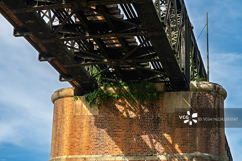 仰视老铁路桥，砖砌桥墩，蓝天背景，展现饱经风霜的金属和自然生长的植物，马来西亚，瓜拉江沙图片素材