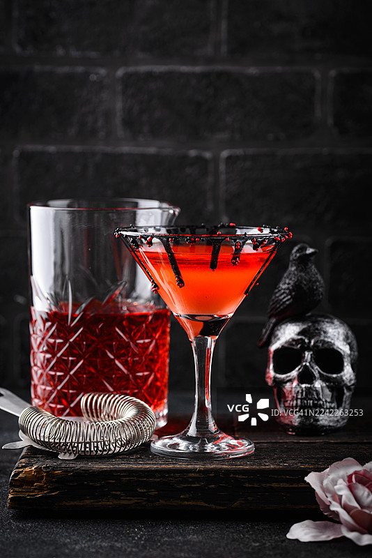 鬼魅万圣节鸡尾酒，配有深色装饰和骷髅头装饰，摆放在质朴的木板上图片素材
