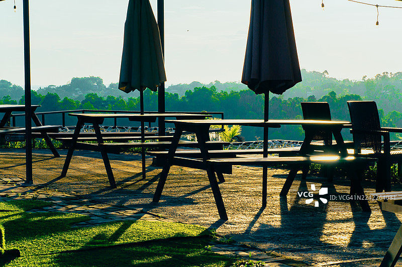 日落时分，空旷的户外餐厅露台，配有桌椅和遮阳伞，俯瞰着葱郁的绿色景观，地点：印度尼西亚三宝垄。图片素材