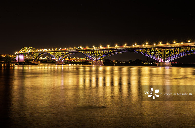 夜晚，灯火辉煌的桥梁横跨宁静的河流，将绚丽的灯光倒映在水面上图片素材