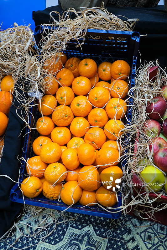 俯视角度拍摄，新鲜的橙子和苹果在充满活力的集市摊位上出售，摆放在稻草中图片素材
