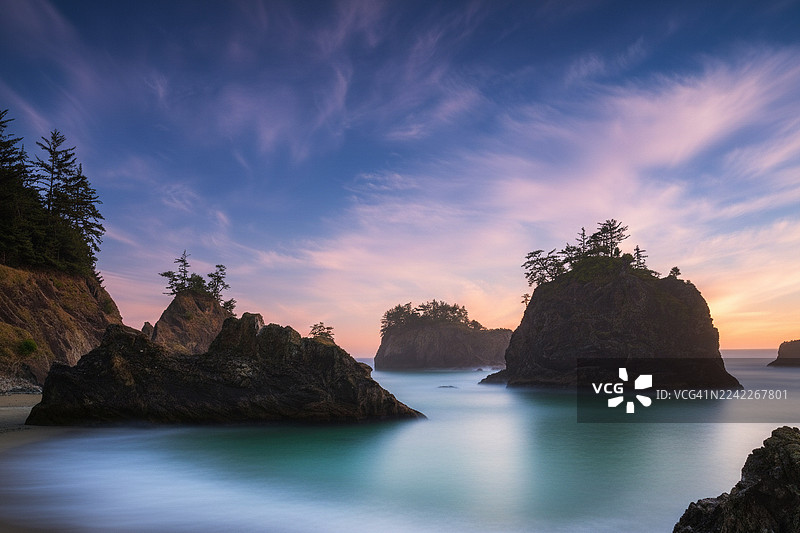 美国俄勒冈州布鲁金斯，秘密海滩步道，宁静海面上方是色彩鲜艳的日落天空，戏剧性的海岸景观与海蚀柱一同构成了一幅宁静而壮丽的自然景象图片素材