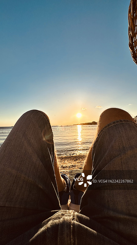 第一人称视角，夕阳下在海滩放松的双腿，背景是海洋和天空图片素材