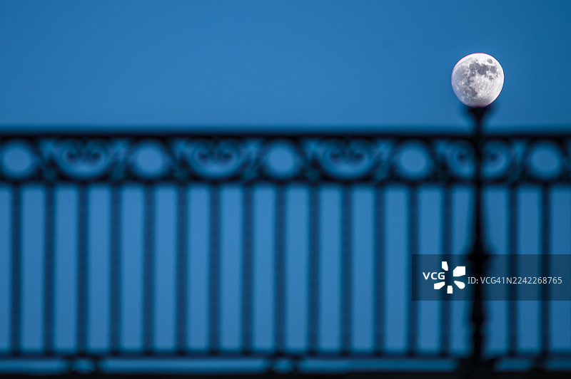 一轮满月从深蓝色夜空中的深色华丽栏杆上方升起，营造出宁静而神秘的氛围，塞维利亚，西班牙，伊莎贝尔二世桥图片素材