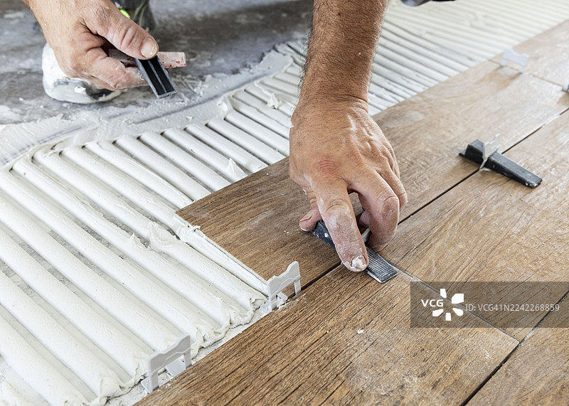 特写：工人的手正在铺设仿木地板瓷砖，使用了胶粘剂和垫片图片素材