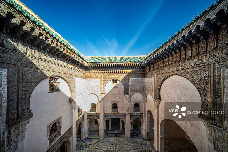 摩洛哥菲斯，Al-Attarine Madrasa庭院的低角度视图，在晴朗的蓝天下展示着精美的伊斯兰建筑，菲斯，摩洛哥图片素材