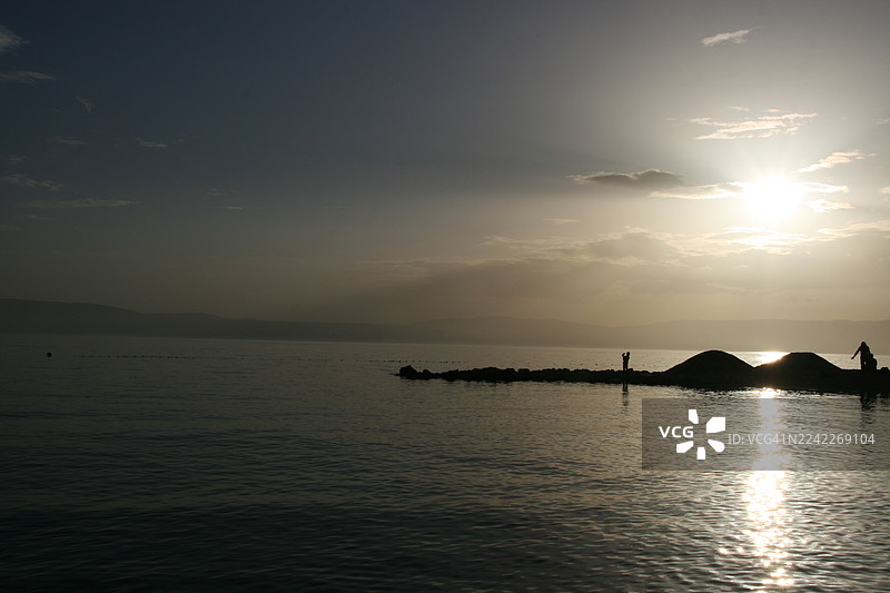 日落时分海滩上的剪影人物，天空色彩鲜艳，水面倒映着景物，克尔克，克罗地亚图片素材