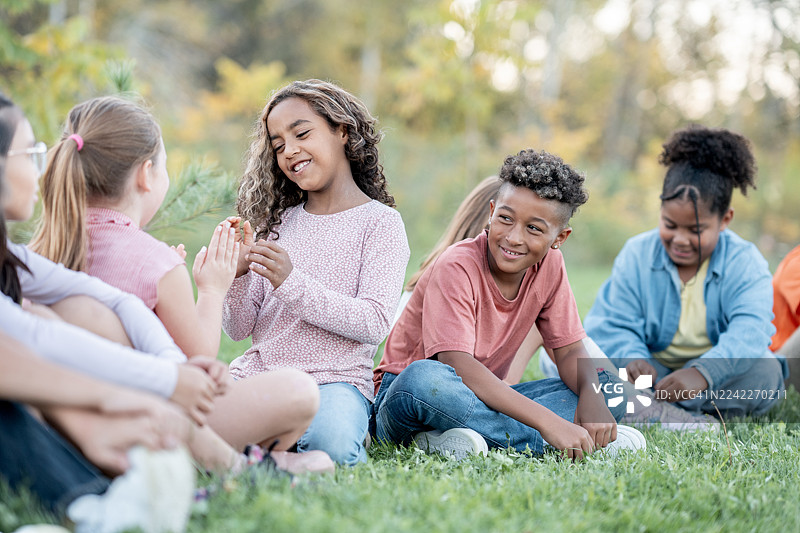 一群不同背景的孩子在公园的户外野餐中愉快地社交，在草地上一起微笑和欢笑图片素材