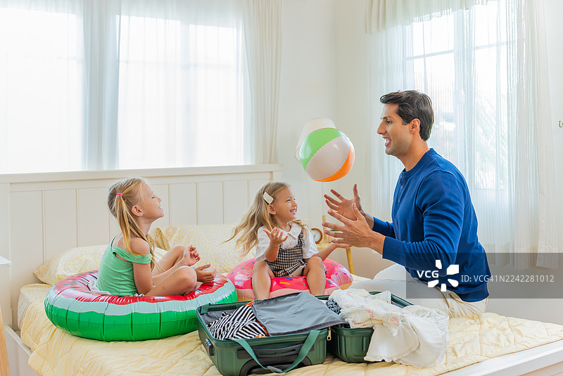 阳光明媚的卧室里，一家三代人（祖父母、父母和孩子）在打包行李时，开心地玩着毛线球和皮箱，进行角色扮演游戏，准备度假。图片素材