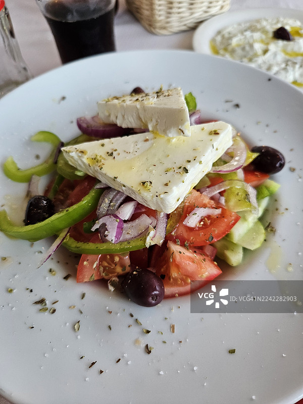 特写镜头，展示一份色彩鲜艳、新鲜的希腊沙拉，配有菲达奶酪、番茄、黄瓜、洋葱、橄榄和青椒，用香草和橄榄油调味，盛放在白盘子上图片素材