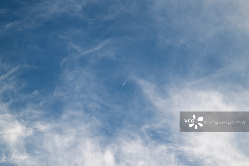 白天时，一弯新月出现在有柔和白云的蓝天上图片素材