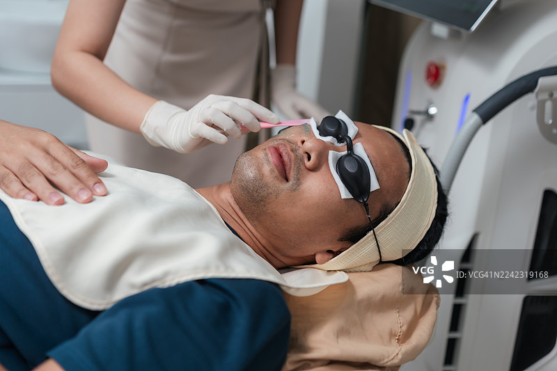 亚洲男性在美容诊所接受美容师的激光嫩肤治疗，为皮肤做好准备，以实现抗衰老和皮肤改善。图片素材