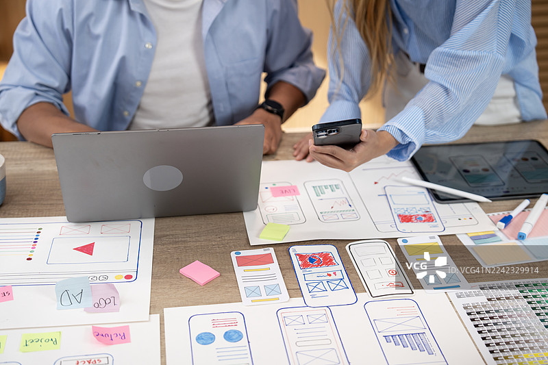 办公室桌上，设计师们近距离协作，绘制手机应用线框图并进行用户体验与界面设计图片素材