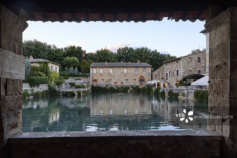 穿过石头拱门看到的巴尼奥维尼奥尼（Bagno Vignoni）的温泉池的镜框视图，意大利托斯卡纳图片素材