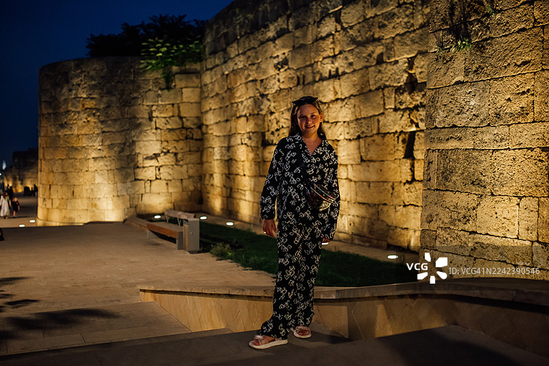夜间街景，一位时尚女子在历史遗迹的古老石墙旁摆姿势。图片素材