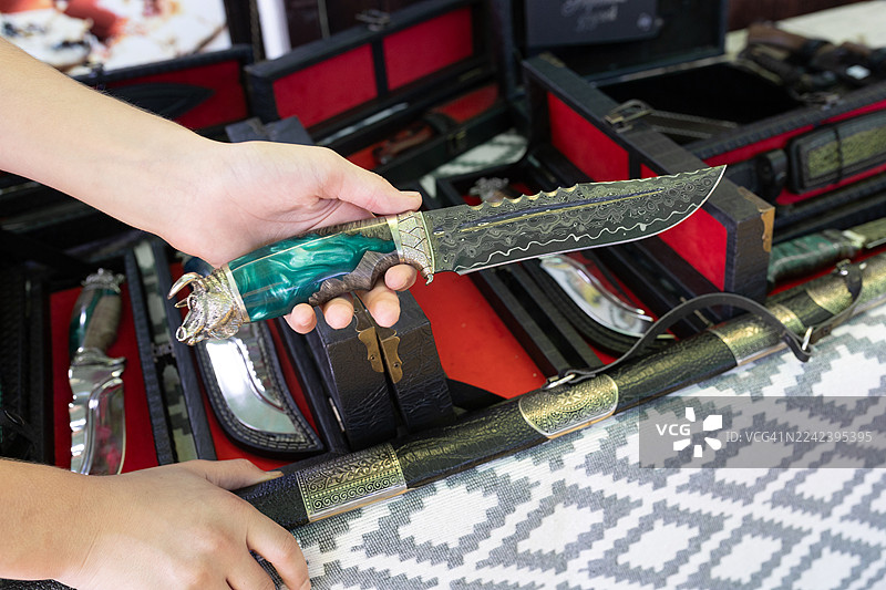 装饰性匕首，饰有华丽的大马士革刀刃和祖母绿手柄，在展柜中被手握持图片素材