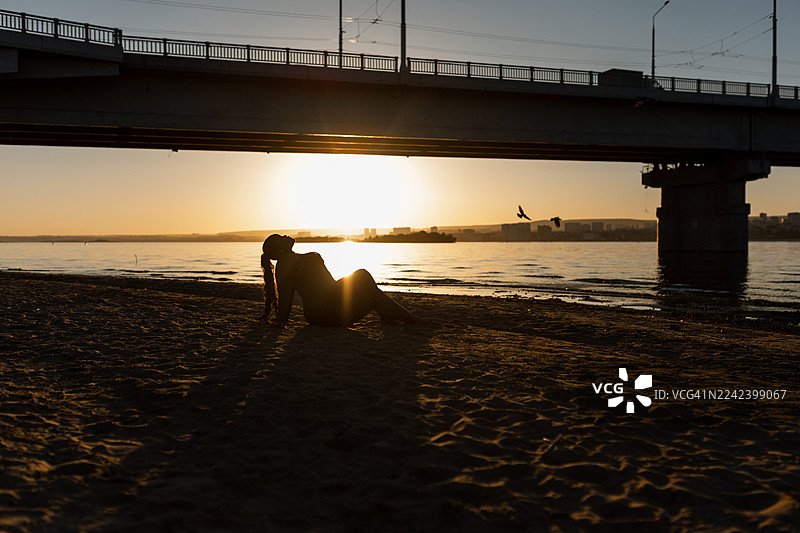 日落时分，一座桥俯瞰着水面，沙滩上一个人的剪影图片素材