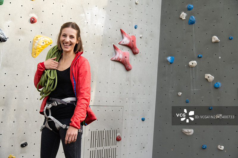 脸上带着微笑的攀岩者在室内岩壁上攀爬，身上带着绳索图片素材