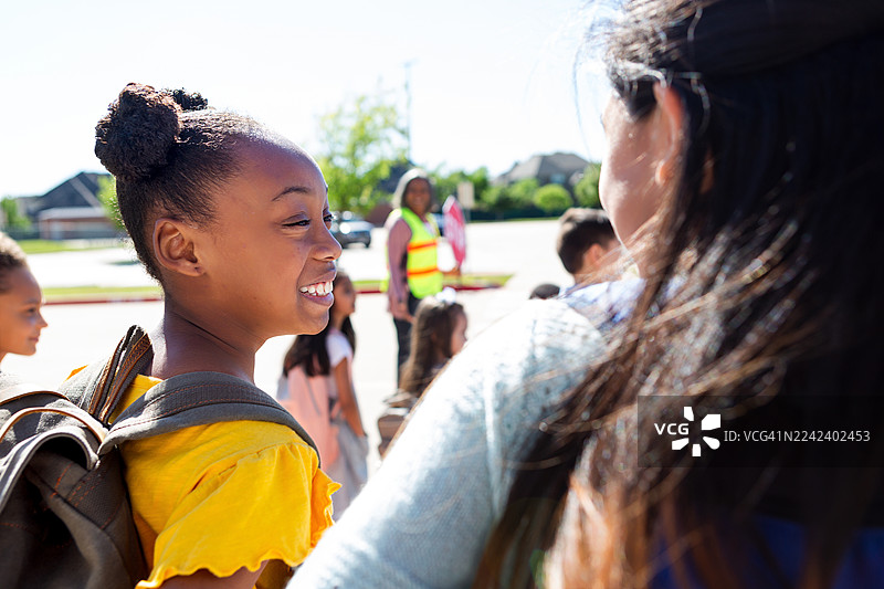 阳光明媚的一天，小女孩在校外与朋友们开心地交谈。图片素材