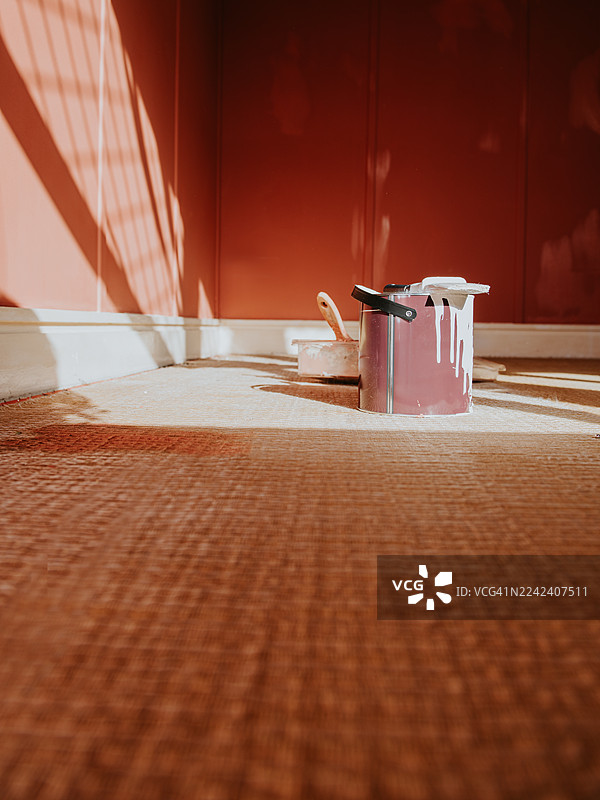 刚粉刷过的房间的广角镜头，墙面颜色是陶土色。油漆刷和凌乱的油漆罐放在墙前的地板上。图片素材