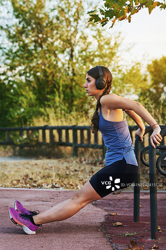 戴着耳机在公园里锻炼肱三头肌的女性图片素材