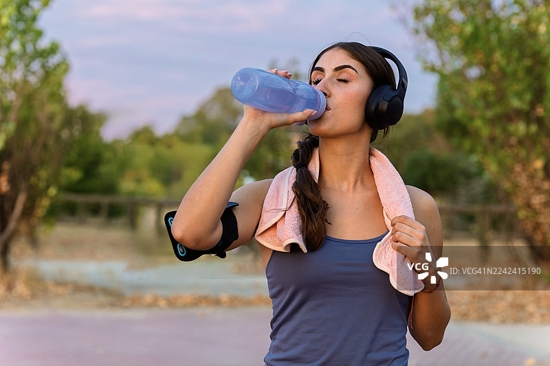 年轻女子在户外运动后，戴着运动耳机补充水分图片素材