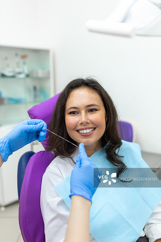 一位开心的患者在明亮的诊所里接受牙科检查，旁边有戴着手套的助手图片素材