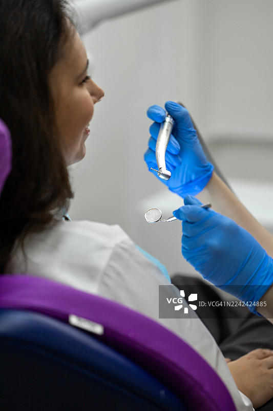 牙医正在为坐在椅子上的患者进行口腔检查，并使用工具。图片素材